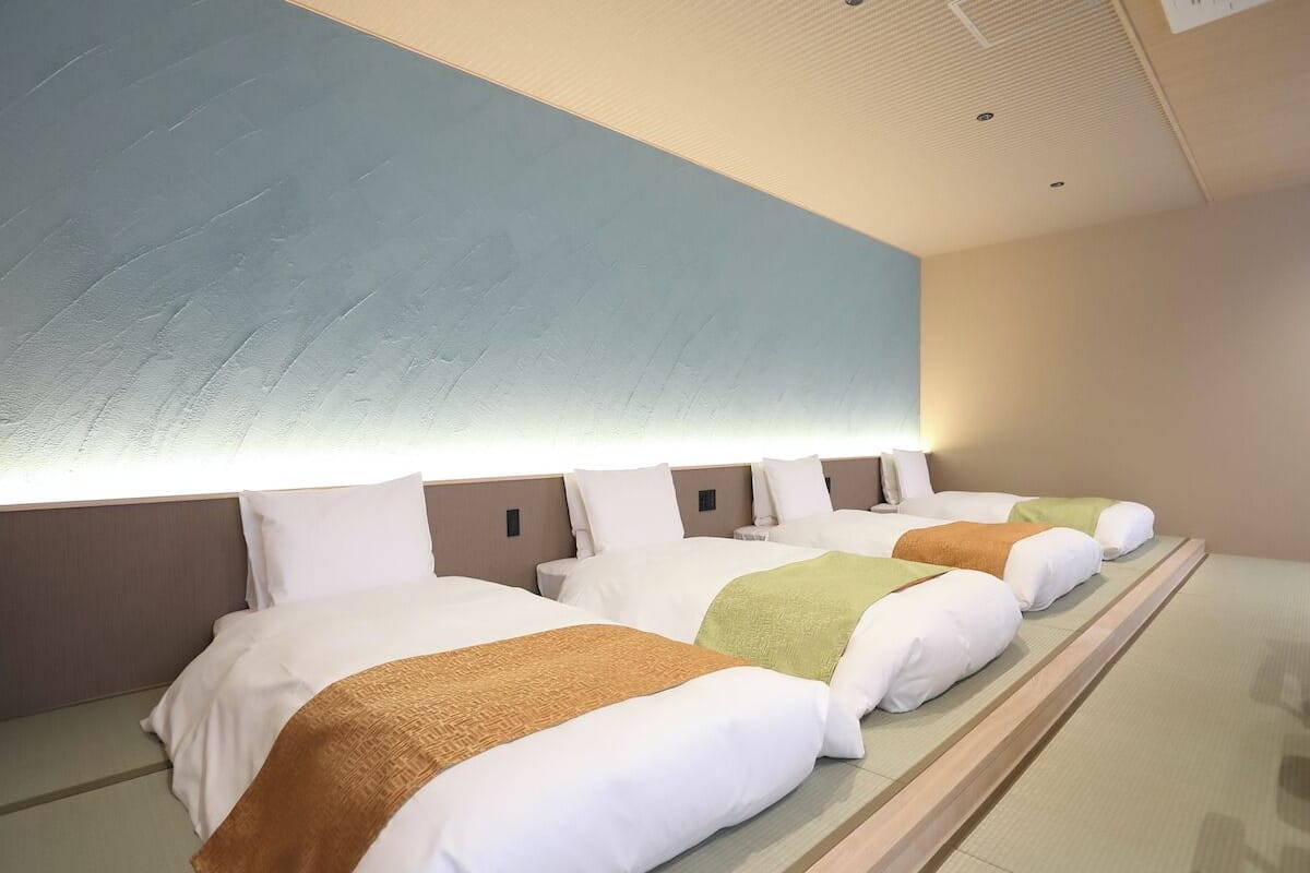 A hotel room with a row of beds, each with a different colored blanket, and a large light fixture above the beds.