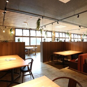 Ein modernes Interieur mit Holztischen und -stühlen, großen Fenstern und hängenden Pflanzen.