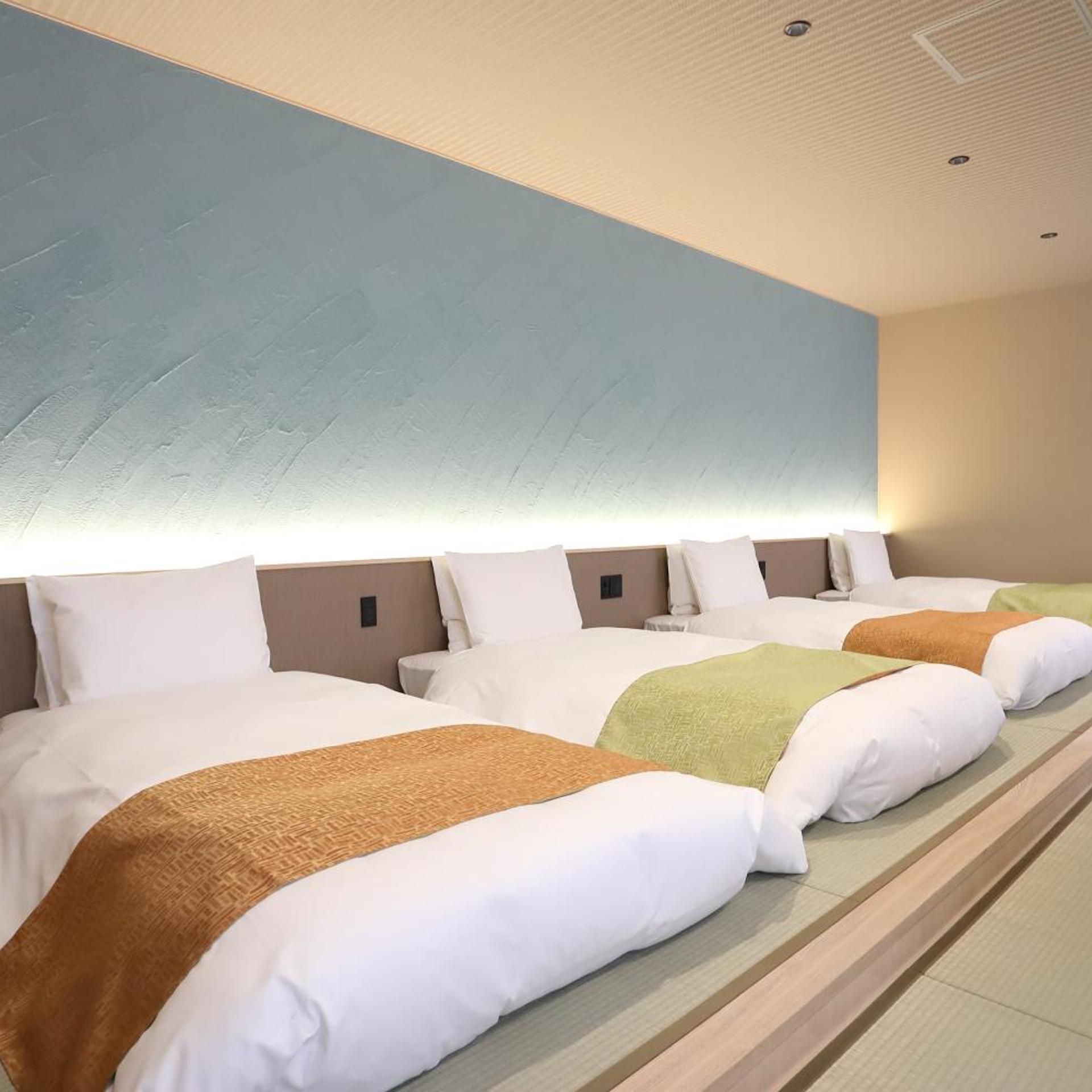 A hotel room with a large bed, a headboard with a light blue panel, and a ceiling with recessed lighting.