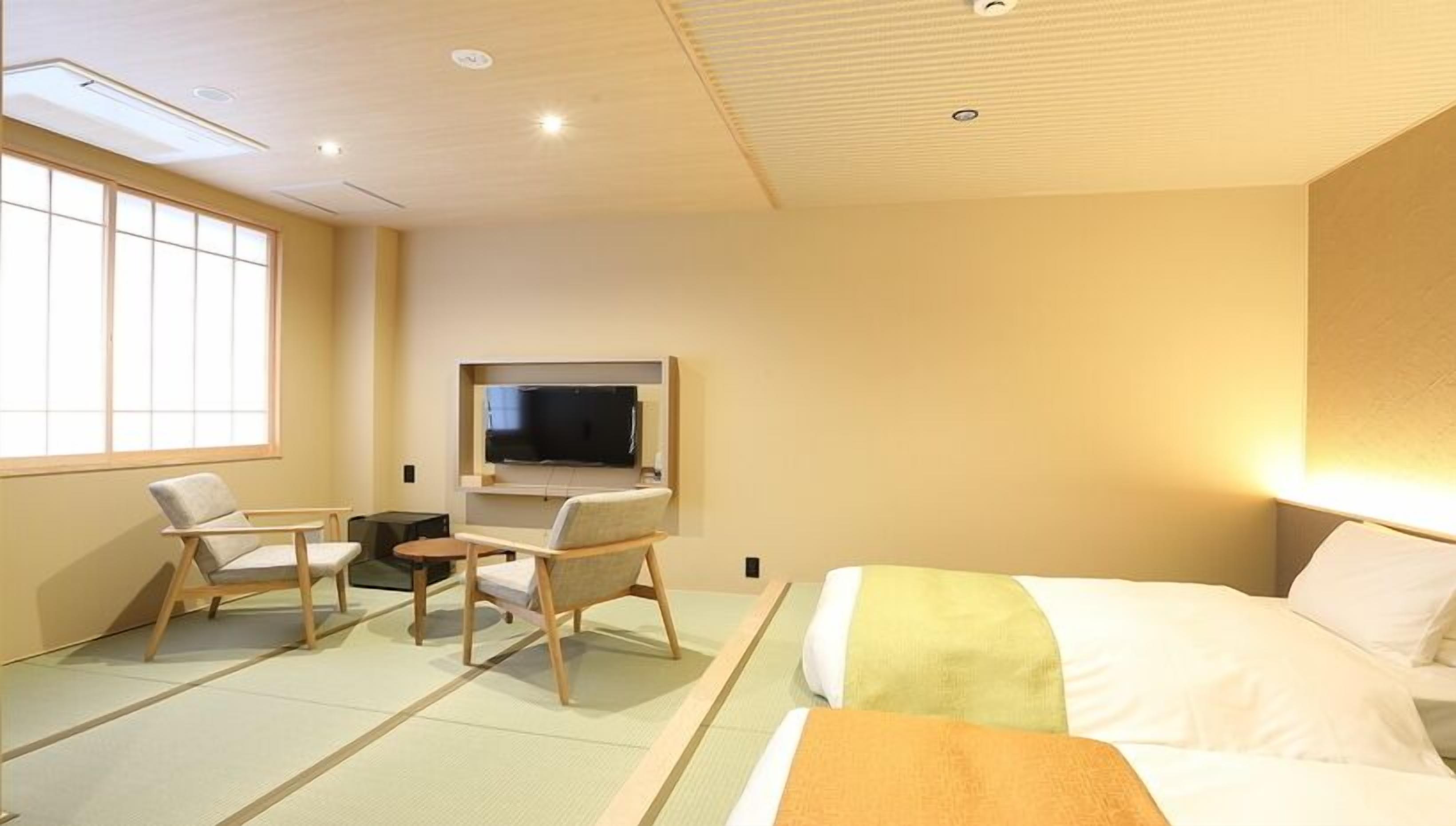A hotel room with tatami flooring, a bed, a TV, and two chairs.