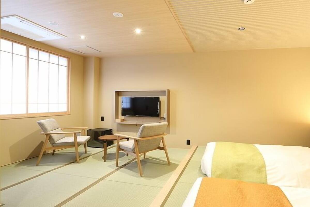 A hotel room with tatami flooring, a bed, a TV, and two chairs.