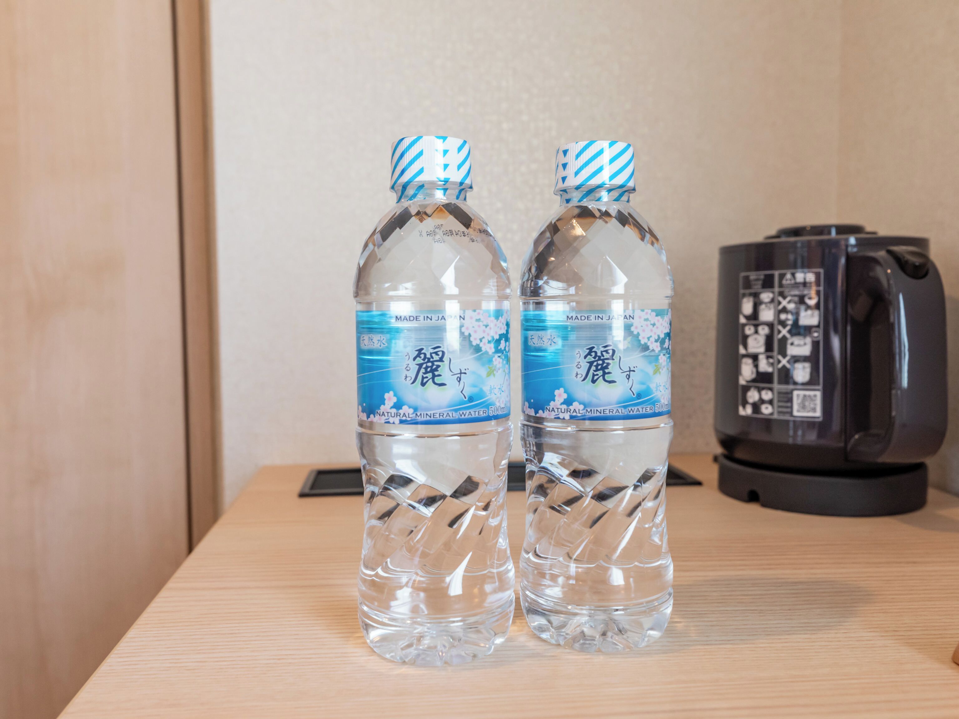 Two bottles of water with labels indicating they are made in Japan, placed on a wooden surface next to a black appliance.