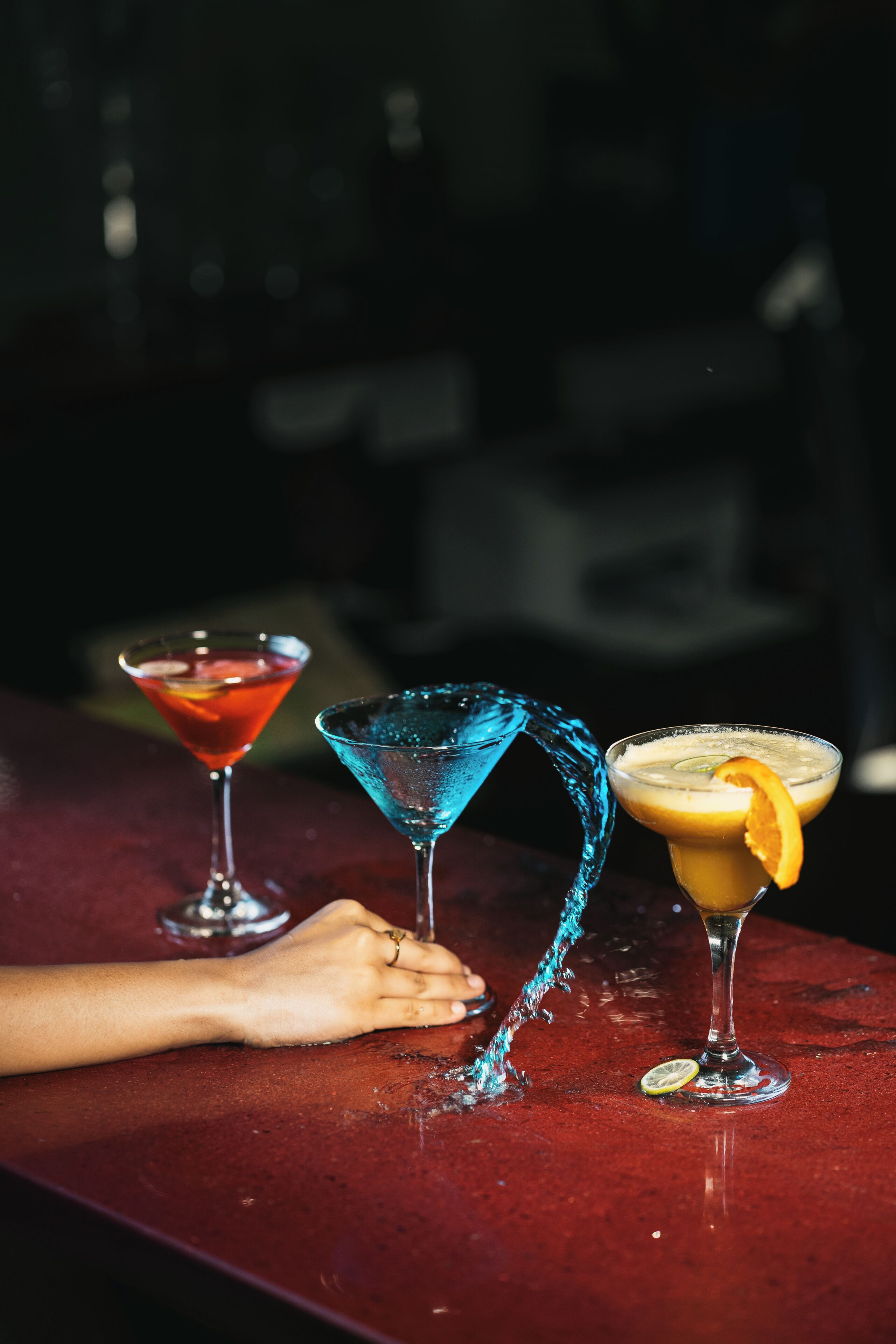 Three cocktails on a bar counter with a hand reaching for one.