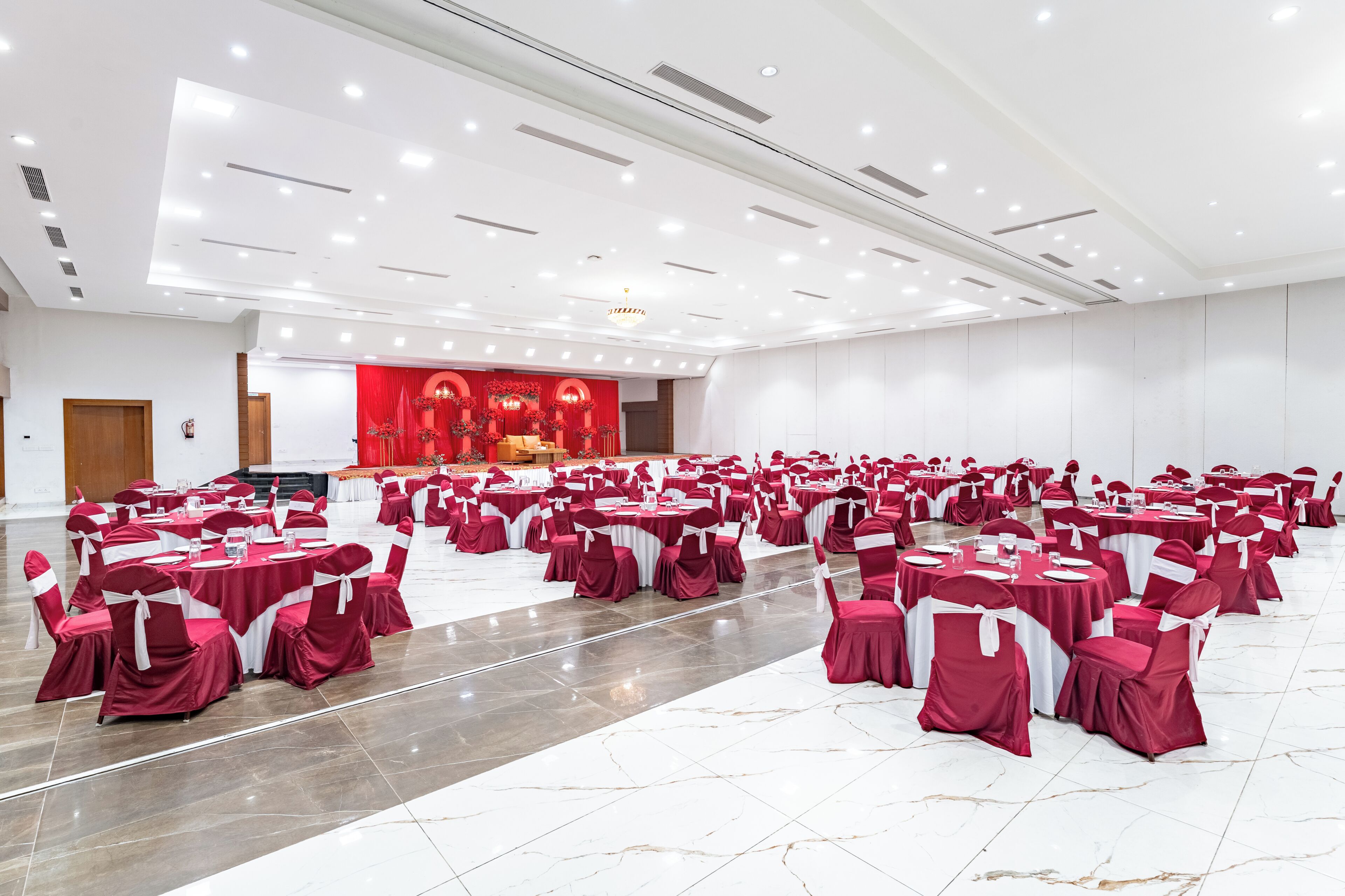 Un amplio salón con filas de mesas y sillas, un escenario con cortinas rojas y un candelabro.