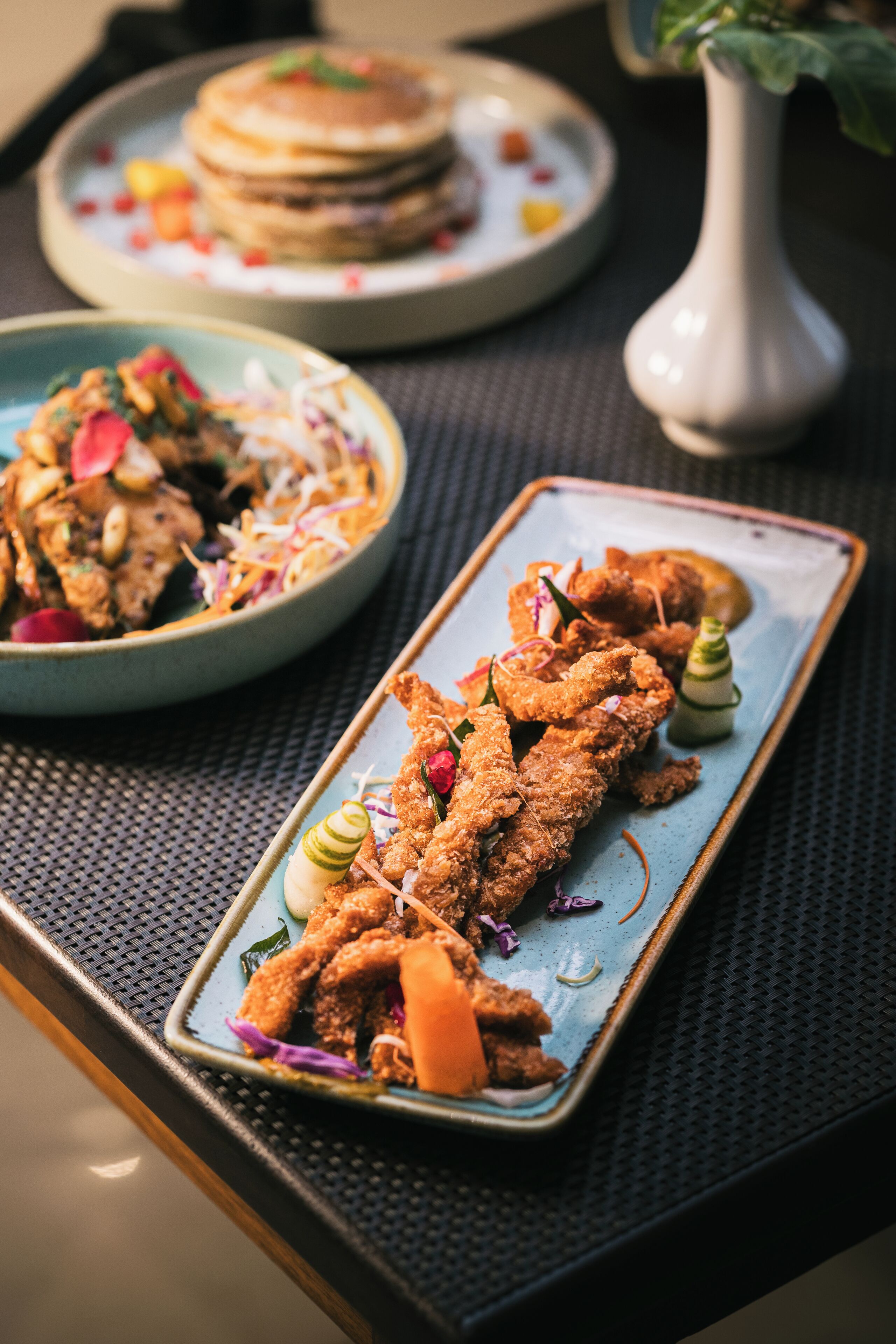 A dining table with a plate of breaded chicken wings garnished with vegetables and a small salad.