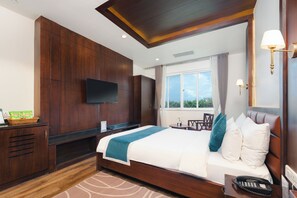 Een hotelkamer met een groot bed, een flatscreen televisie aan de muur, een bureau met een mand lekkernijen en een raam met gordijnen.
