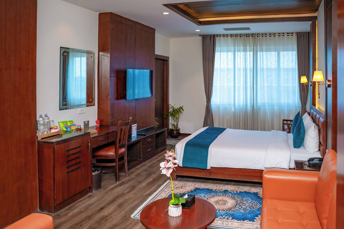 Een hotelkamer met een bed, een bureau, een stoel, een televisie en een tafeltje met een bloemenvaas.