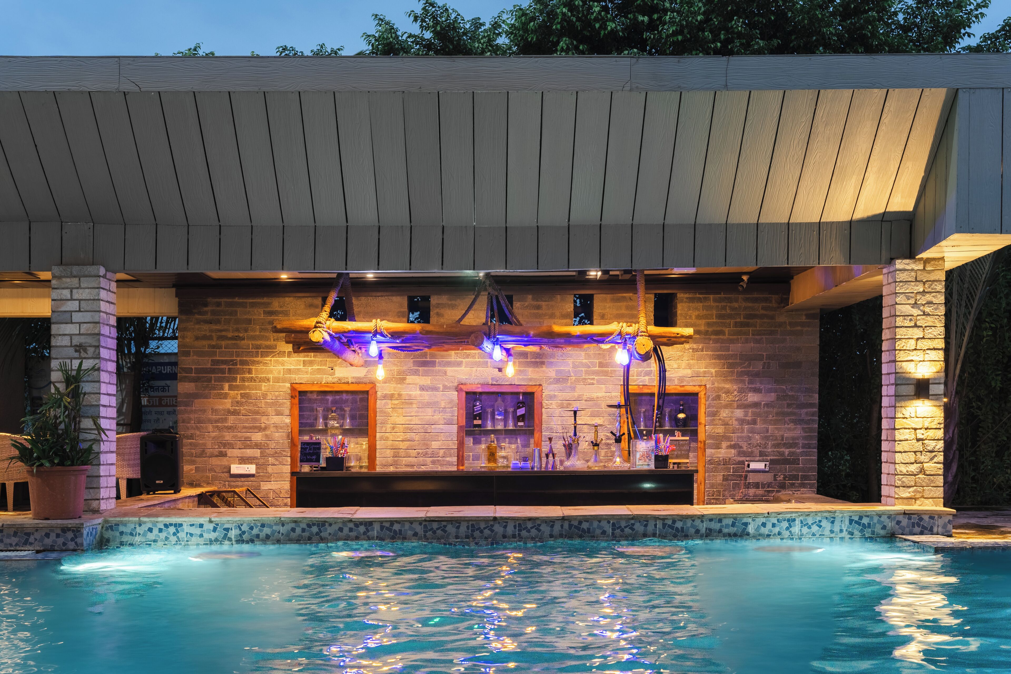 Zona de bar junto a la piscina, con pared de ladrillo, techo de madera y una piscina de agua cristalina.