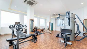A modern gym with various exercise equipment, large windows, and a wooden floor.