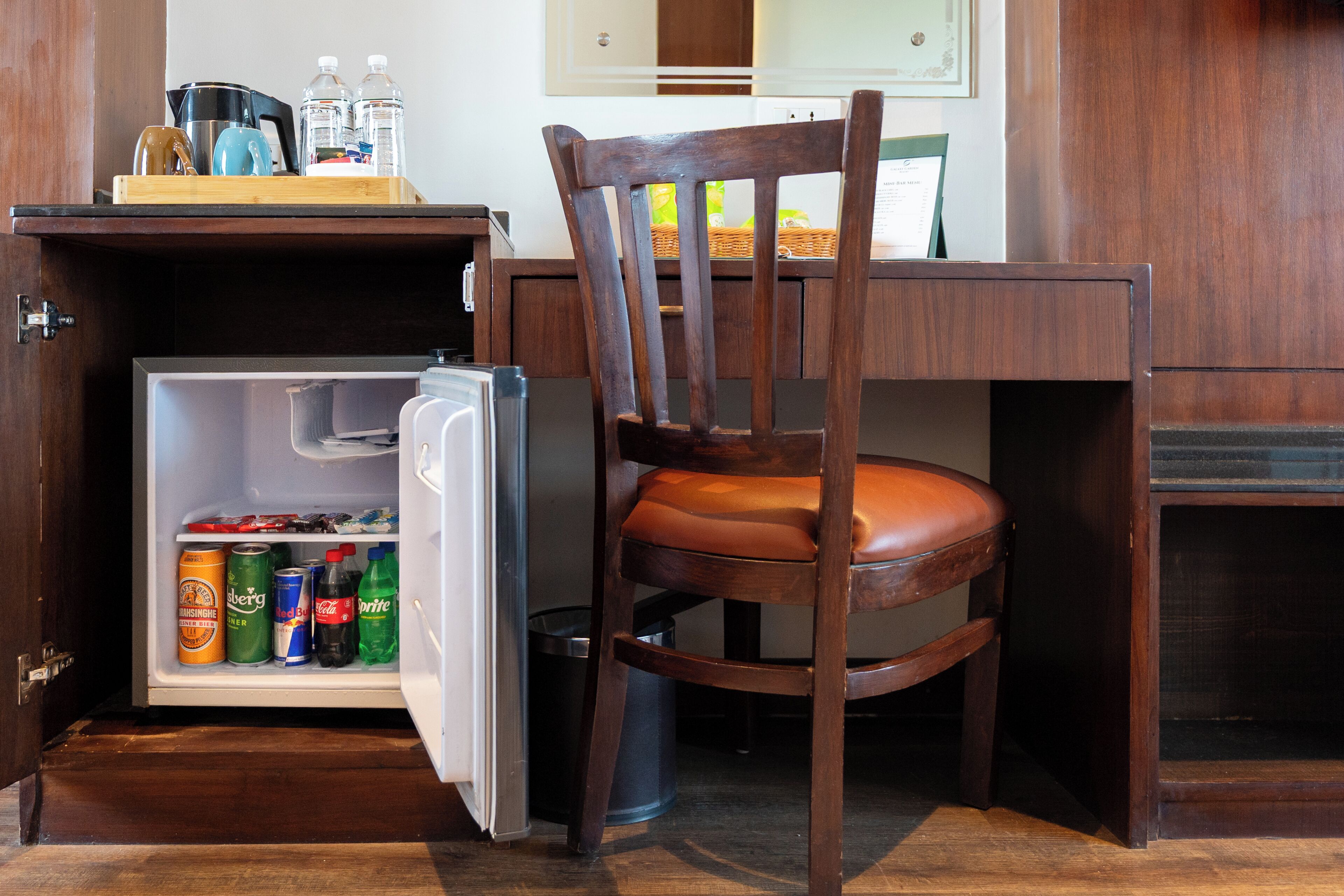 Una kitchenette compacta con refrigerador, una silla de madera y una pequeña mesa con hervidor y botellas de agua.