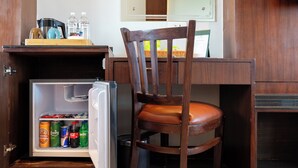 Une petite cuisine équipée comprenant un réfrigérateur, une chaise en bois et une petite table avec une bouilloire et des bouteilles d’eau.