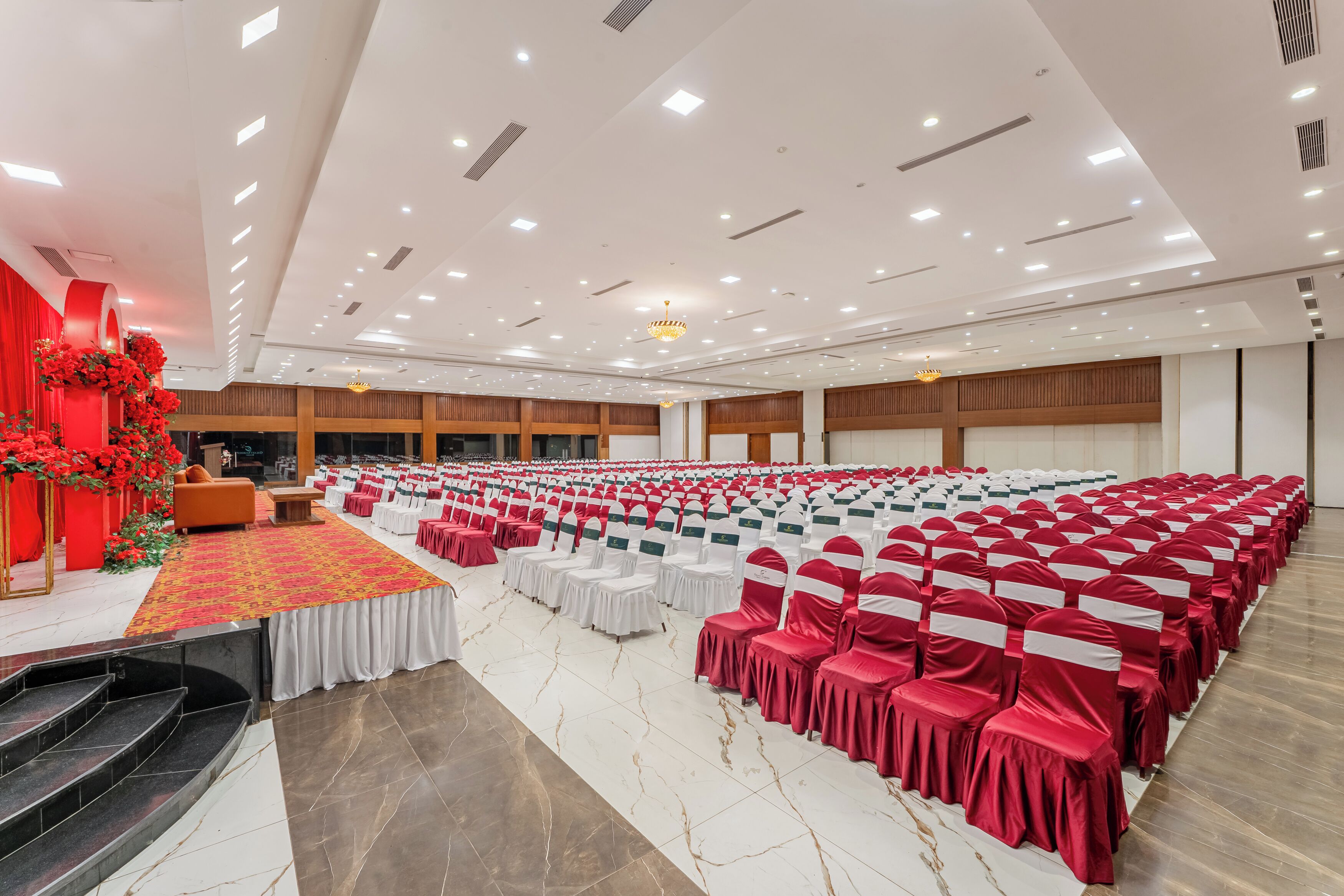 Un salón amplio con filas de sillas, un escenario con cortinas rojas y una escalera.