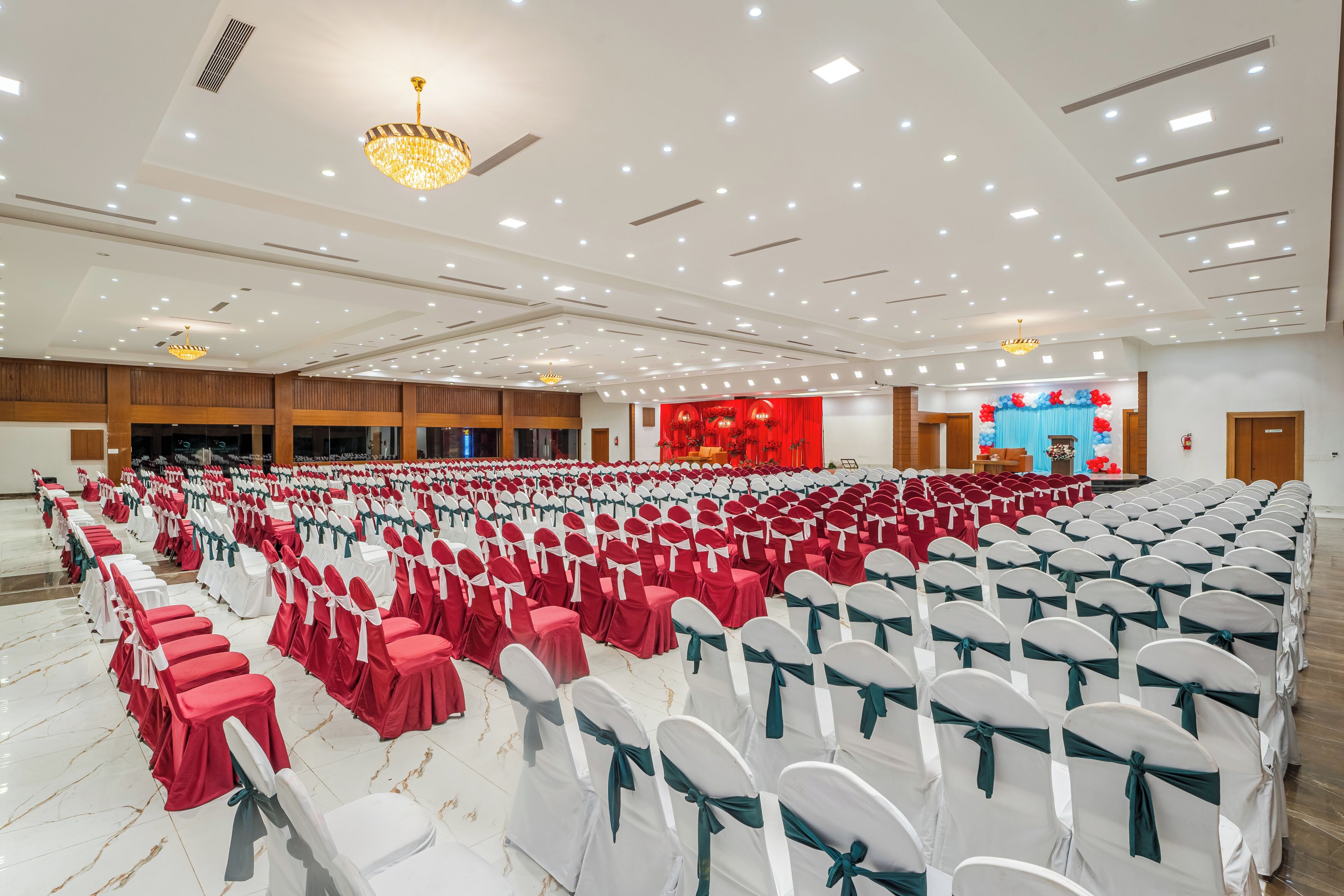 A large hall with rows of chairs, some covered in red and others in white, and a stage with red curtains in the background.