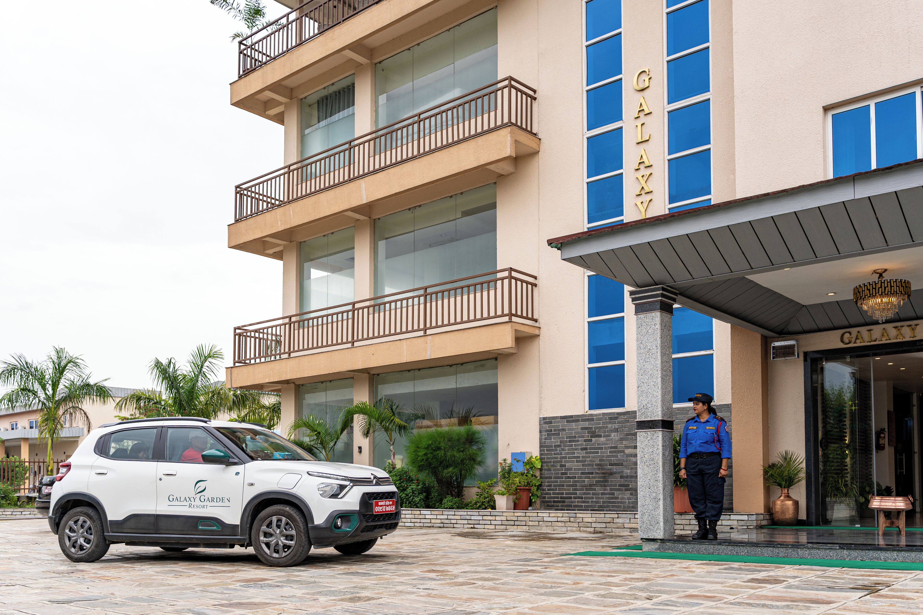 Un hotel a più piani con un cartello che riporta la scritta 'GALAXY' e un SUV bianco parcheggiato di fronte.