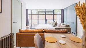 A modern hotel room with a large bed, a seating area with a table, and a view of the outside. - Hackney 1 Bed Garden Flat Sleeps 4 Adults (London)