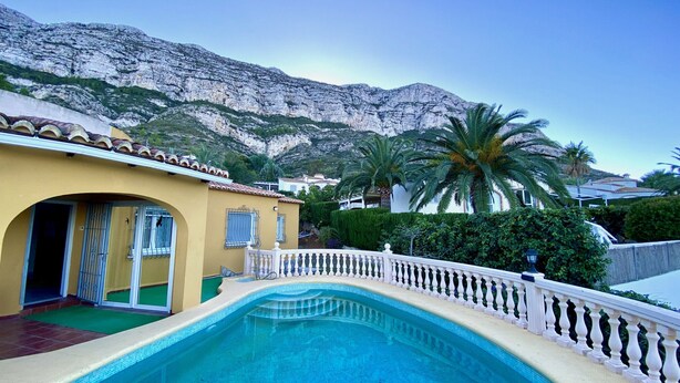 A swimming pool with a white balustrade, a yellow building with a tiled roof, and a mountainous backdrop. - Villa Canoa-3-d vistas al mar , piscina MT003 (Denia)