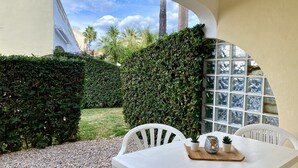 Eine Terrasse mit weißem Tisch und Stühlen, umgeben von einer Hecke und einer Mauer aus Glasbausteinen.