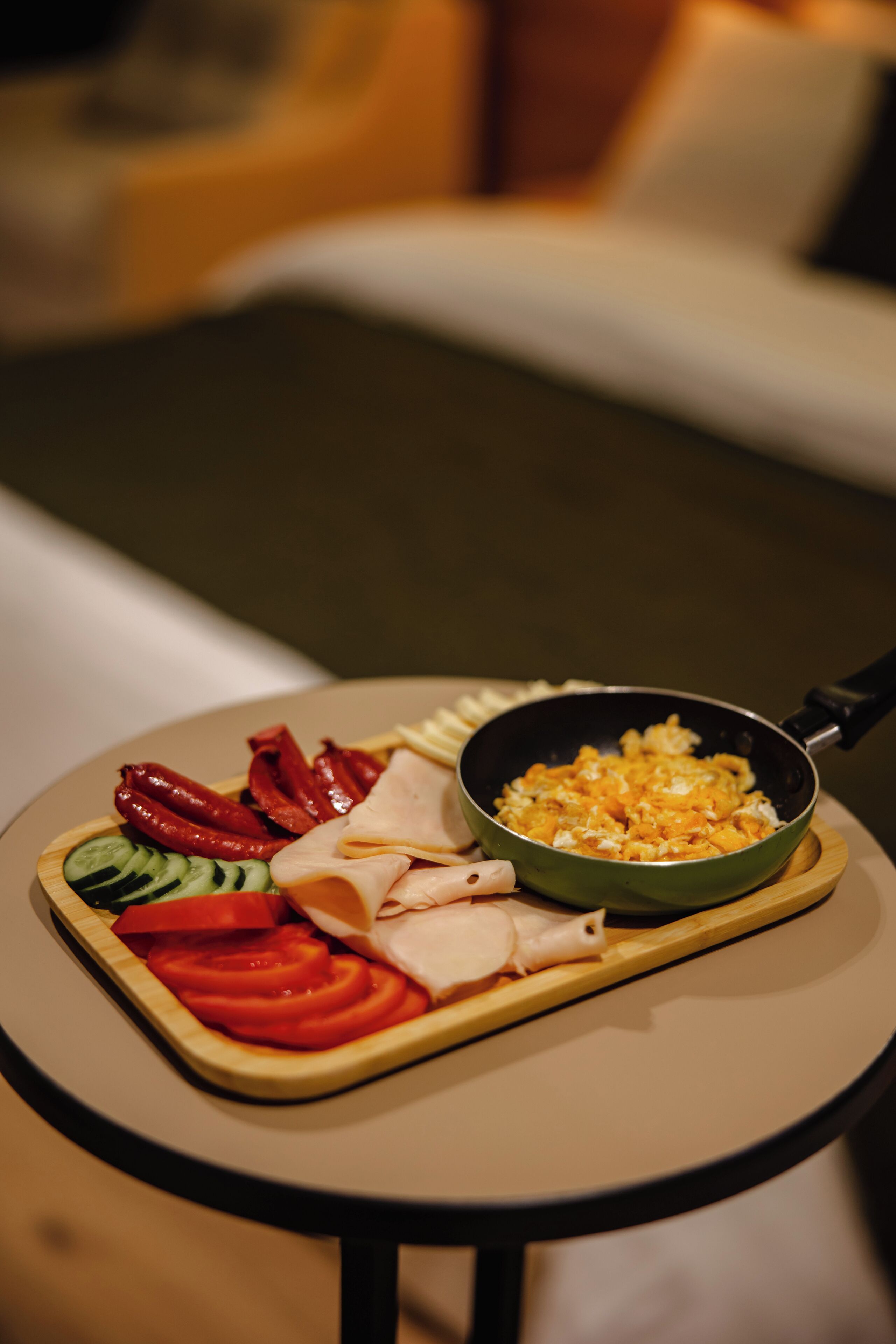 Una mesa de comedor con diversos alimentos, como tomates en rodajas, pepinos, pimientos rojos y carne, junto con una sartén con huevos revueltos.