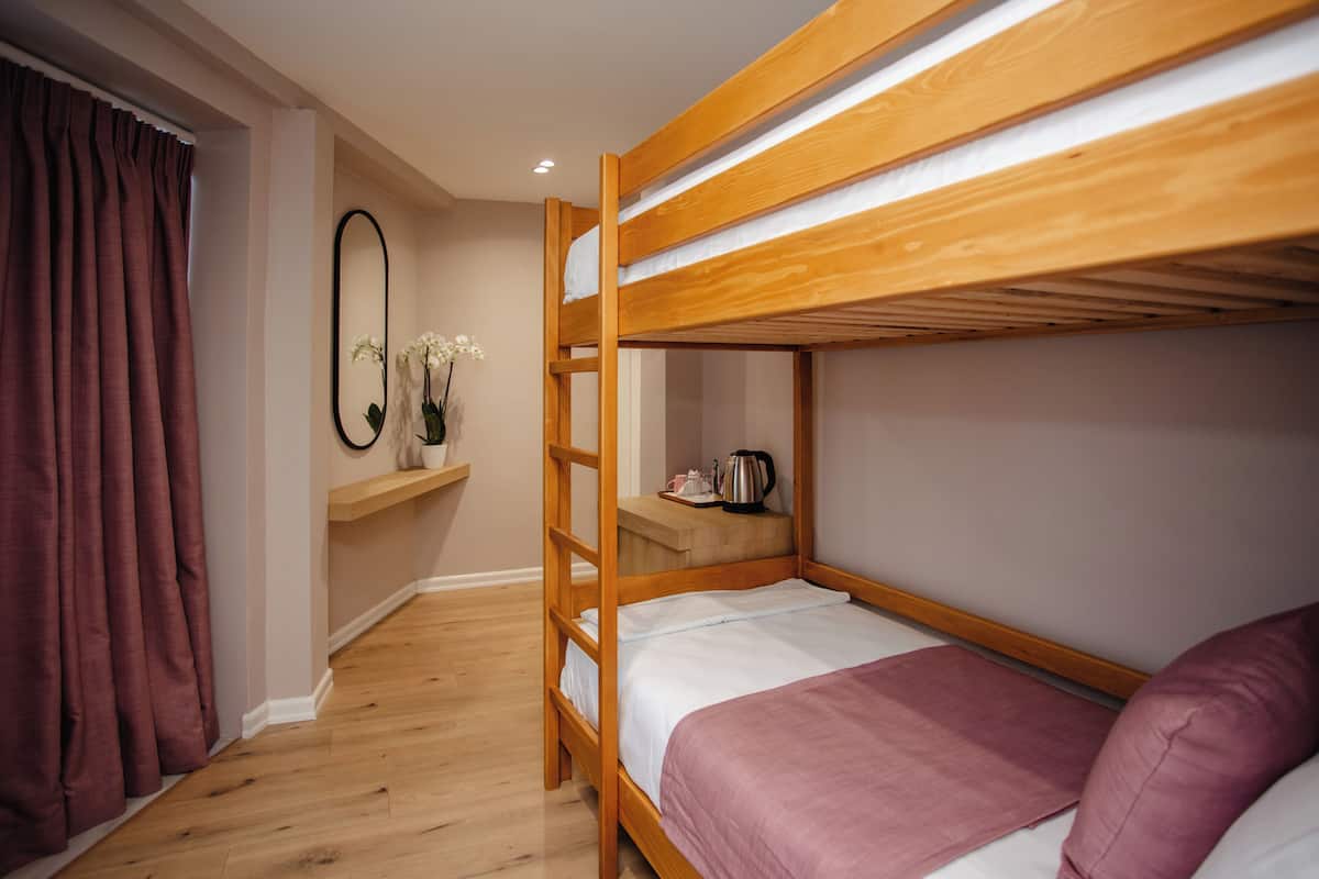 A bunk bed room with a wooden frame, a shelf with a mirror, and a small table with a kettle.