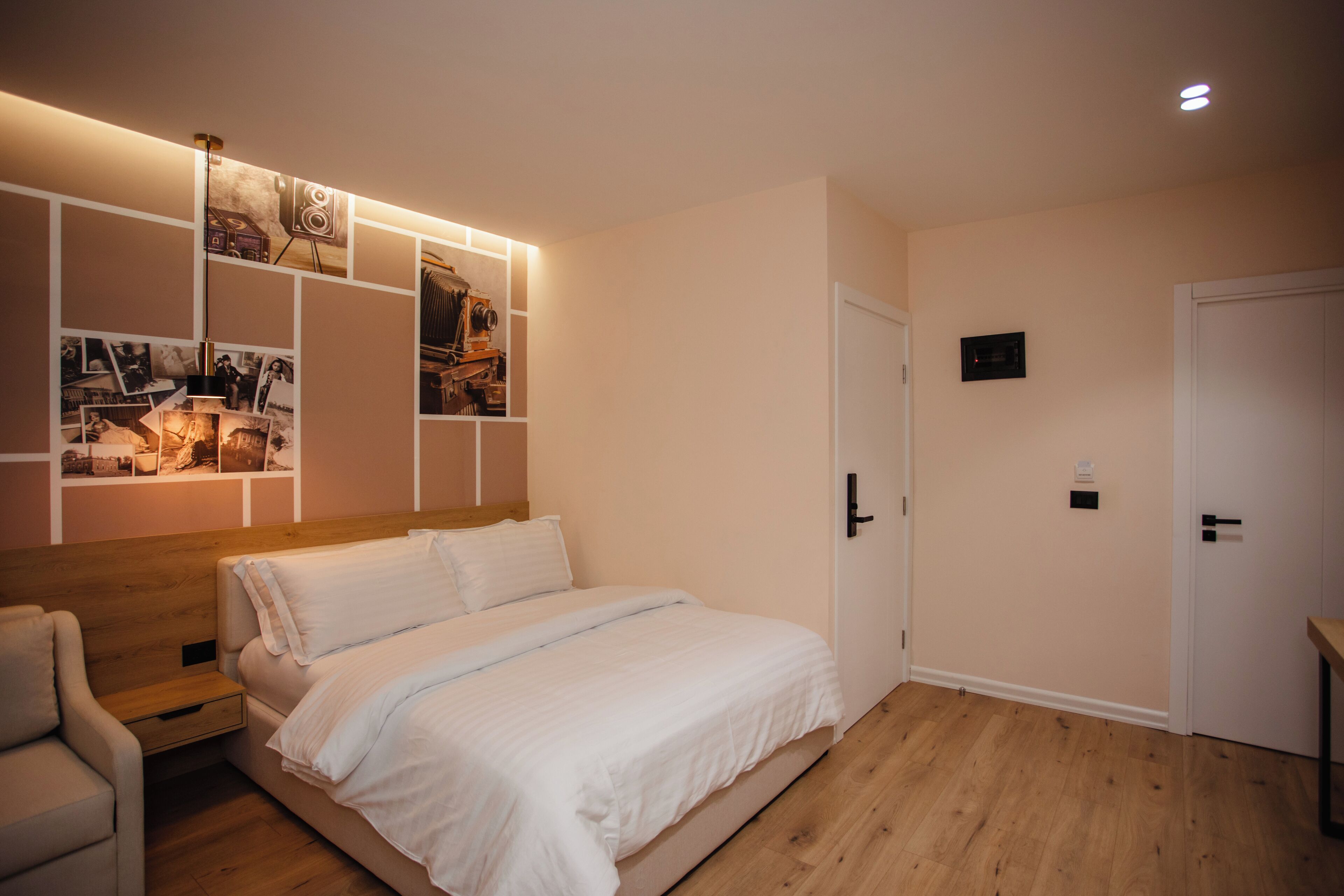 Un dormitorio con una cama de madera, una mesita de noche, una silla, un estante en la pared con fotografías y una puerta con manija.
