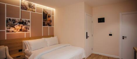 Un dormitorio con una cama de madera, una mesita de noche, una silla, un estante en la pared con fotografías y una puerta con manija.