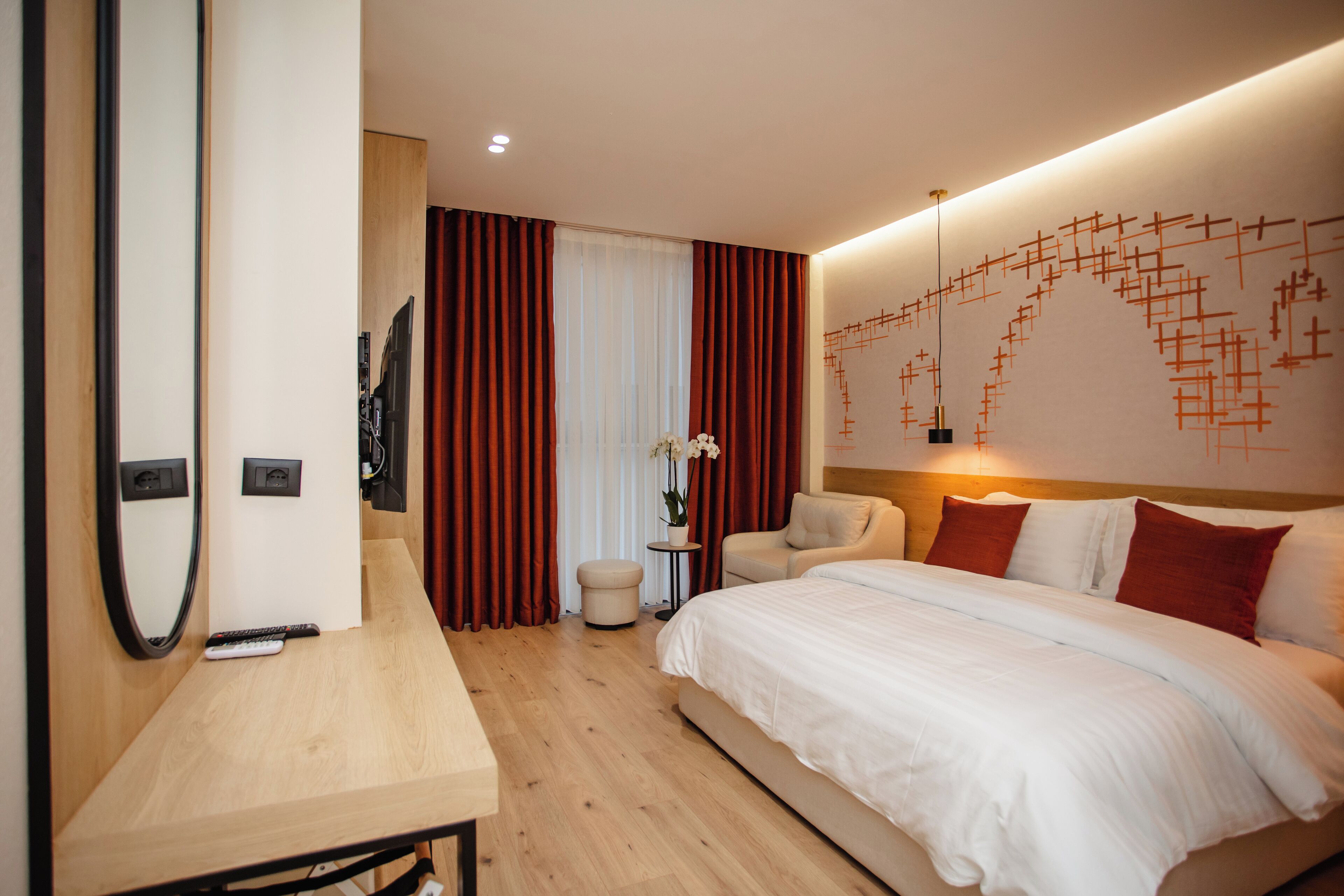 A modern hotel room with a large bed, a desk, a chair, and a small table.