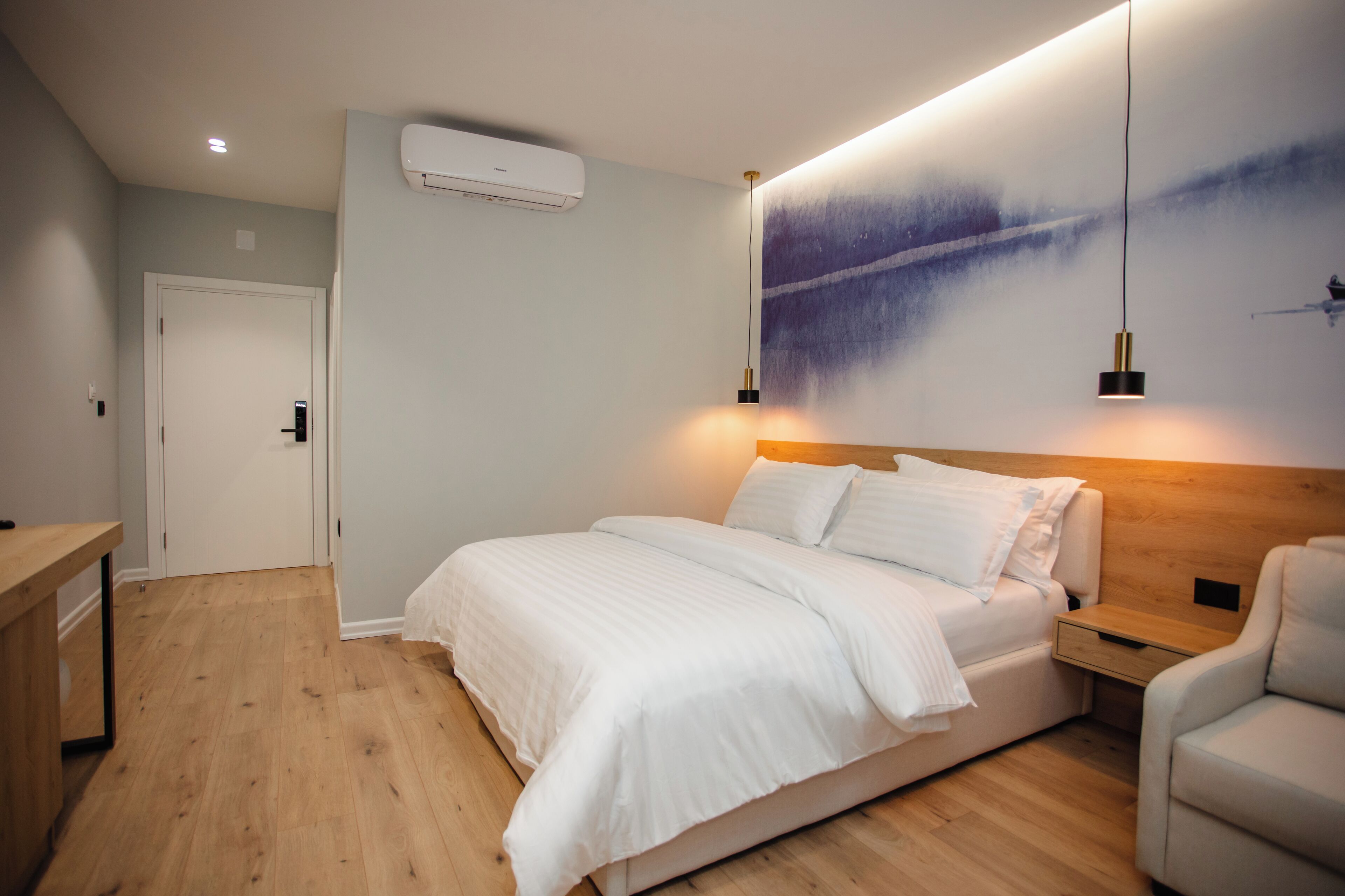 Una camera da letto moderna con pavimento in legno, un letto con biancheria bianca, un comodino, una sedia e un condizionatore d'aria a parete.