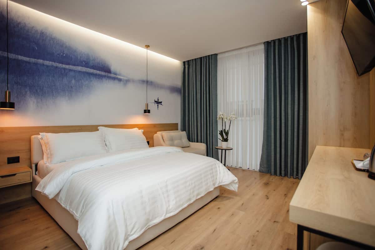 A modern bedroom with a large bed, bedside tables, a desk, and a wall-mounted TV.