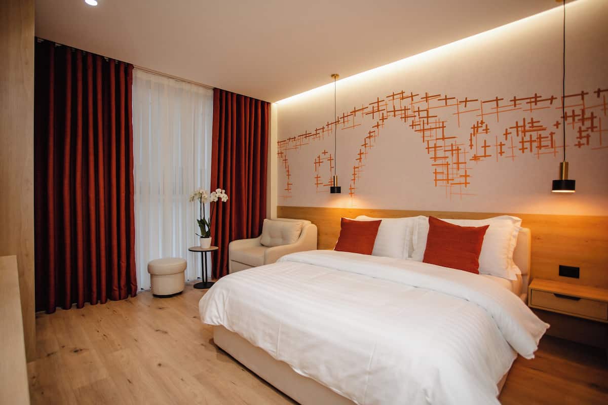 A modern hotel room with a large bed, a nightstand, a chair, and a wall art piece.