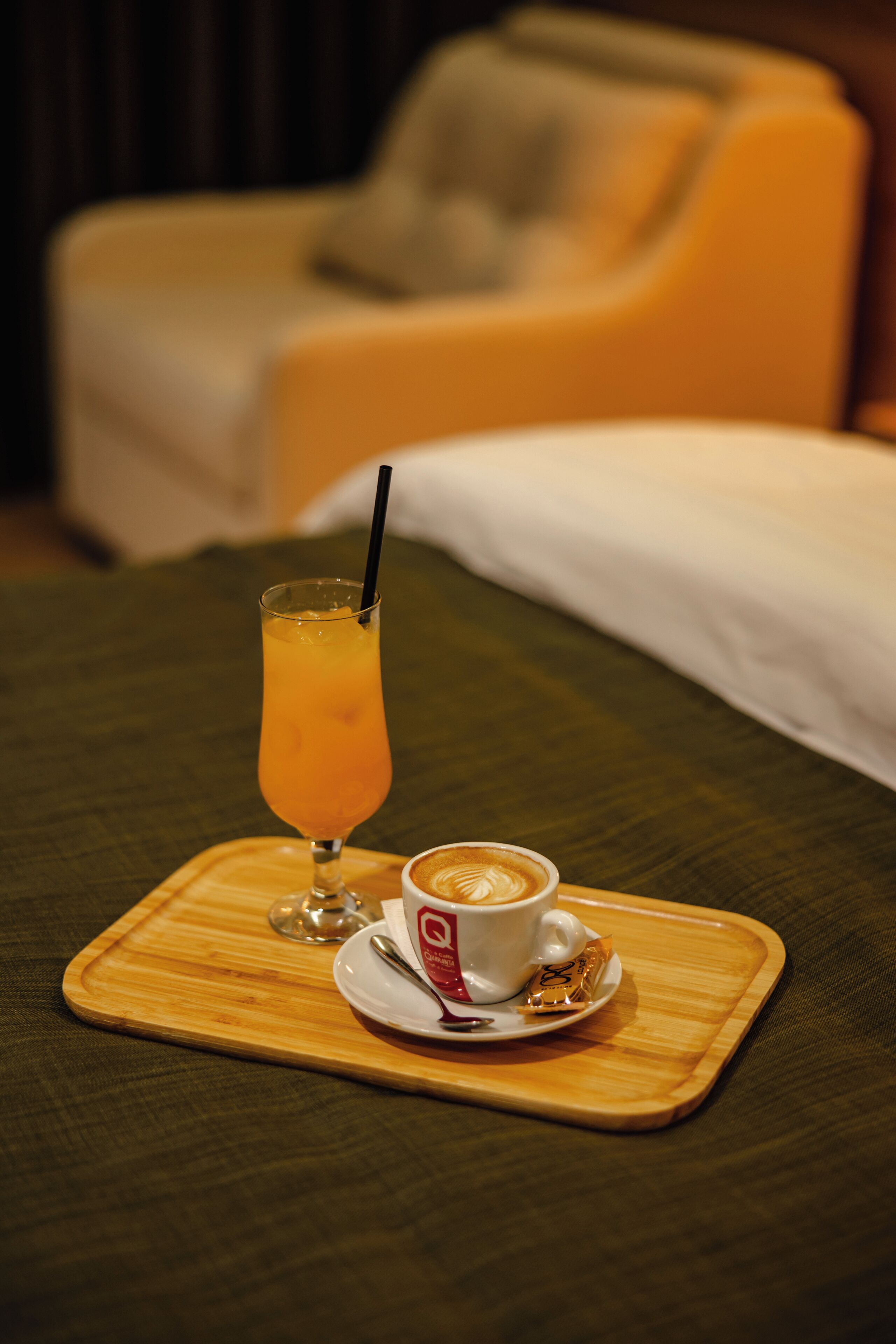 A tray with a glass of orange juice and a cup of coffee on a bed.