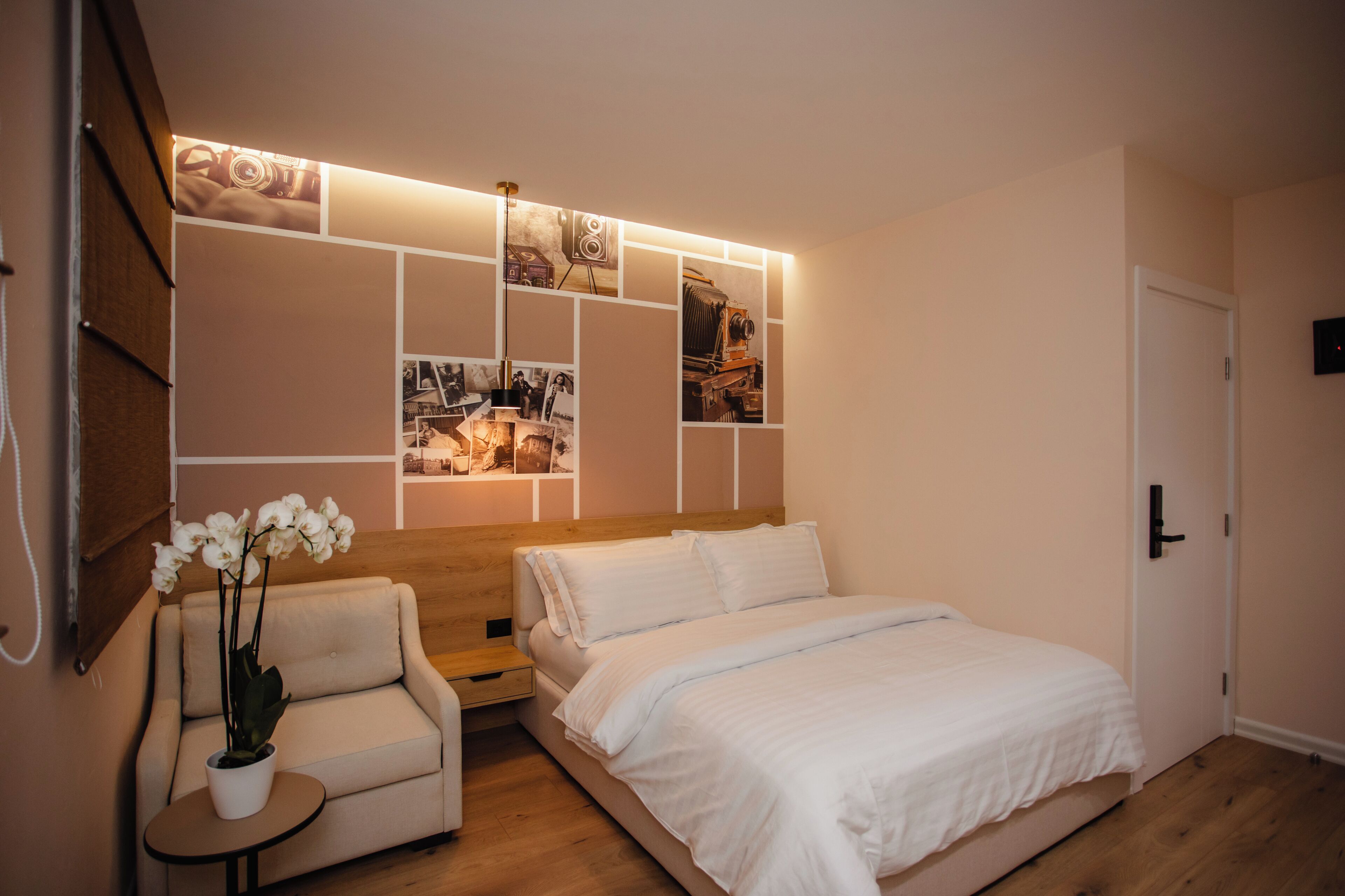 A bedroom with a bed, a small sofa, a nightstand, a wall-mounted shelf with photos, and a potted plant.