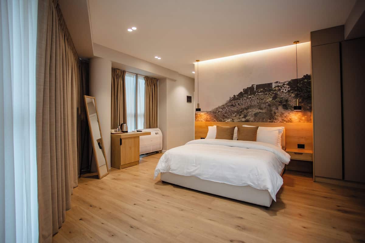 A modern bedroom with a large bed, a desk, and a wall-mounted artwork.