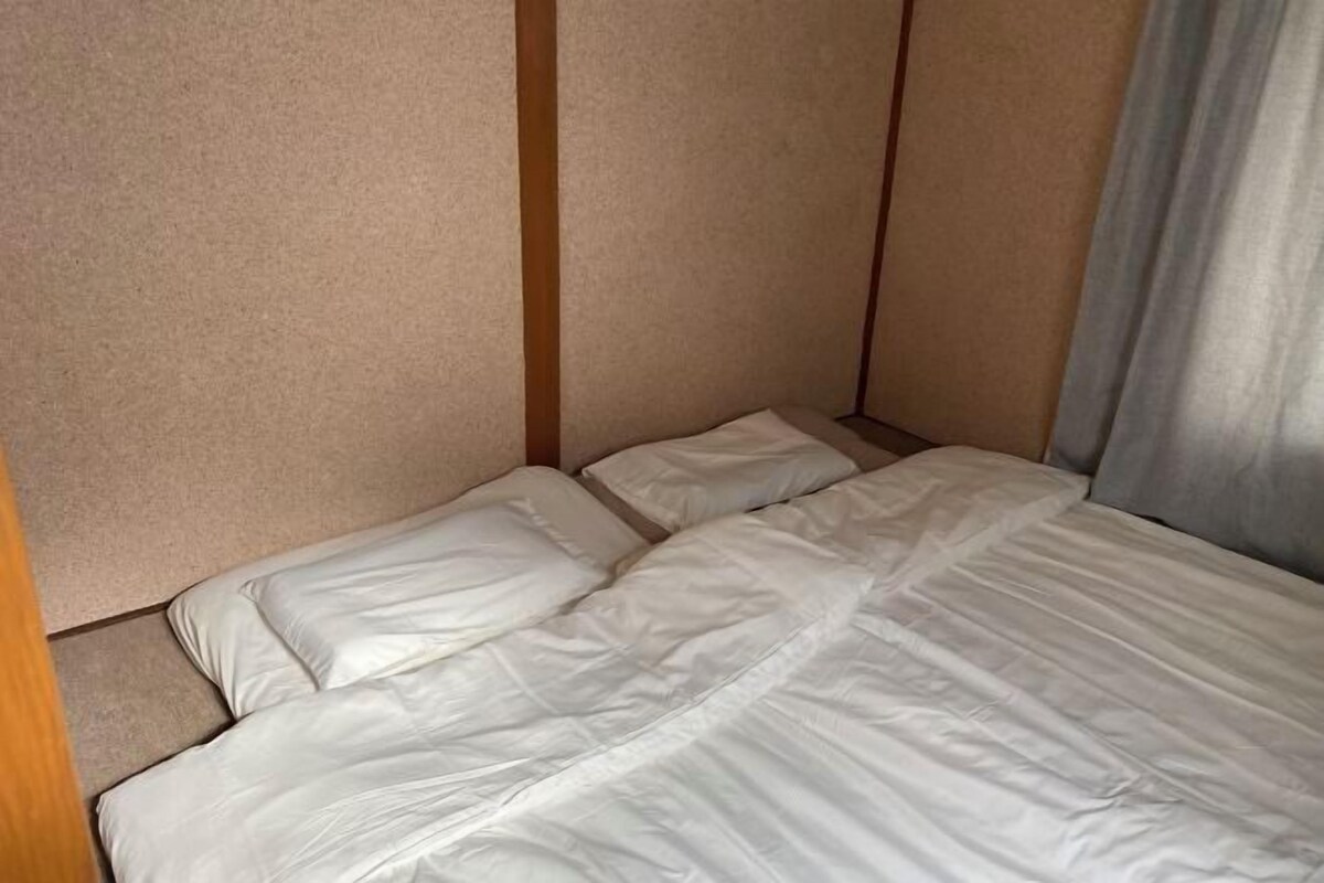 Un lit simple avec une literie blanche, dans une pièce aux murs de couleur beige et dotée d’une tête de lit en bois.