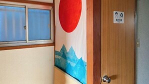 Une pièce avec une porte en bois, une fenêtre à vitrage dépoli et un mur orné d’un cercle rouge et d’un tableau représentant une montagne.
