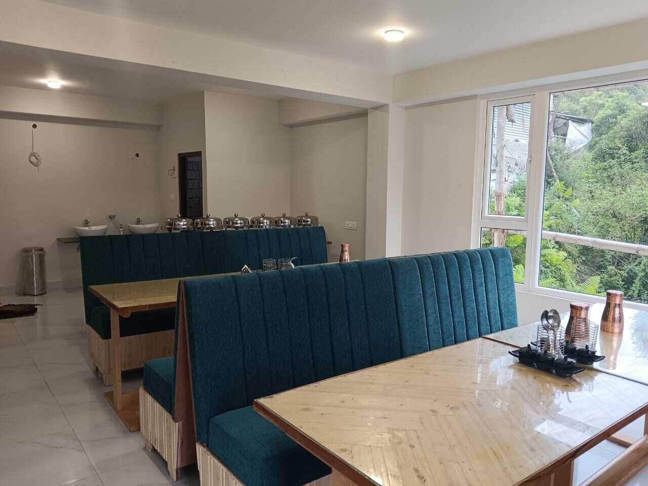 A dining area with wooden tables and blue upholstered booths, a kitchen counter with utensils, and a view of greenery through the window.