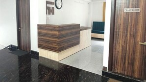 A reception area with a wooden reception desk, a clock on the wall, and a sign indicating a wash room. - FLORET RESORT LACHUNG (Chungthang)