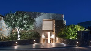 A modern building with a stone facade, a large window with horizontal blinds, and a paved entrance area with lights. - Villa Sendal with Stunning Views to Spinalonga & Elounda Bay (Neapoli)