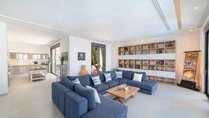 A modern living room with a sectional sofa, a wooden coffee table, and a bookshelf filled with decorative items. - Villa Sendal with Stunning Views to Spinalonga & Elounda Bay (Neapoli)