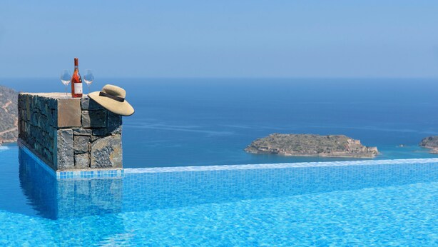 A poolside view with a stone ledge, a bottle, and a hat. - Villa Sendal with Stunning Views to Spinalonga & Elounda Bay (Neapoli)