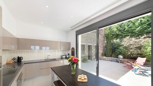 A modern kitchen with a large island, a view of the garden, and outdoor seating. - Villa Sendal with Stunning Views to Spinalonga & Elounda Bay (Neapoli)