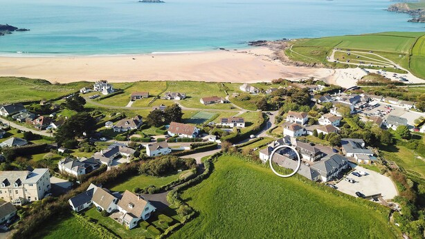 An aerial view of a coastal residential area with houses, a beach, and a small island in the distance. - Attractive cottage two minute walk to the beach, dog friendly, parking (Harlyn)