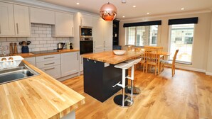 A modern kitchen with wooden countertops, a central island, bar stools, and a dining area with a table and chairs. - Attractive cottage two minute walk to the beach, dog friendly, parking (Harlyn)