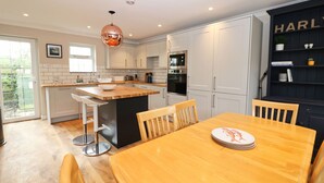 A modern kitchen with white cabinets, a wooden dining table, and a built-in island. - Attractive cottage two minute walk to the beach, dog friendly, parking (Harlyn)