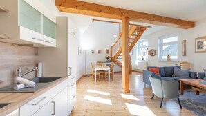 Een moderne keuken met houten balken, een eethoek met een trap en een woonkamer met een bank en een tafel.