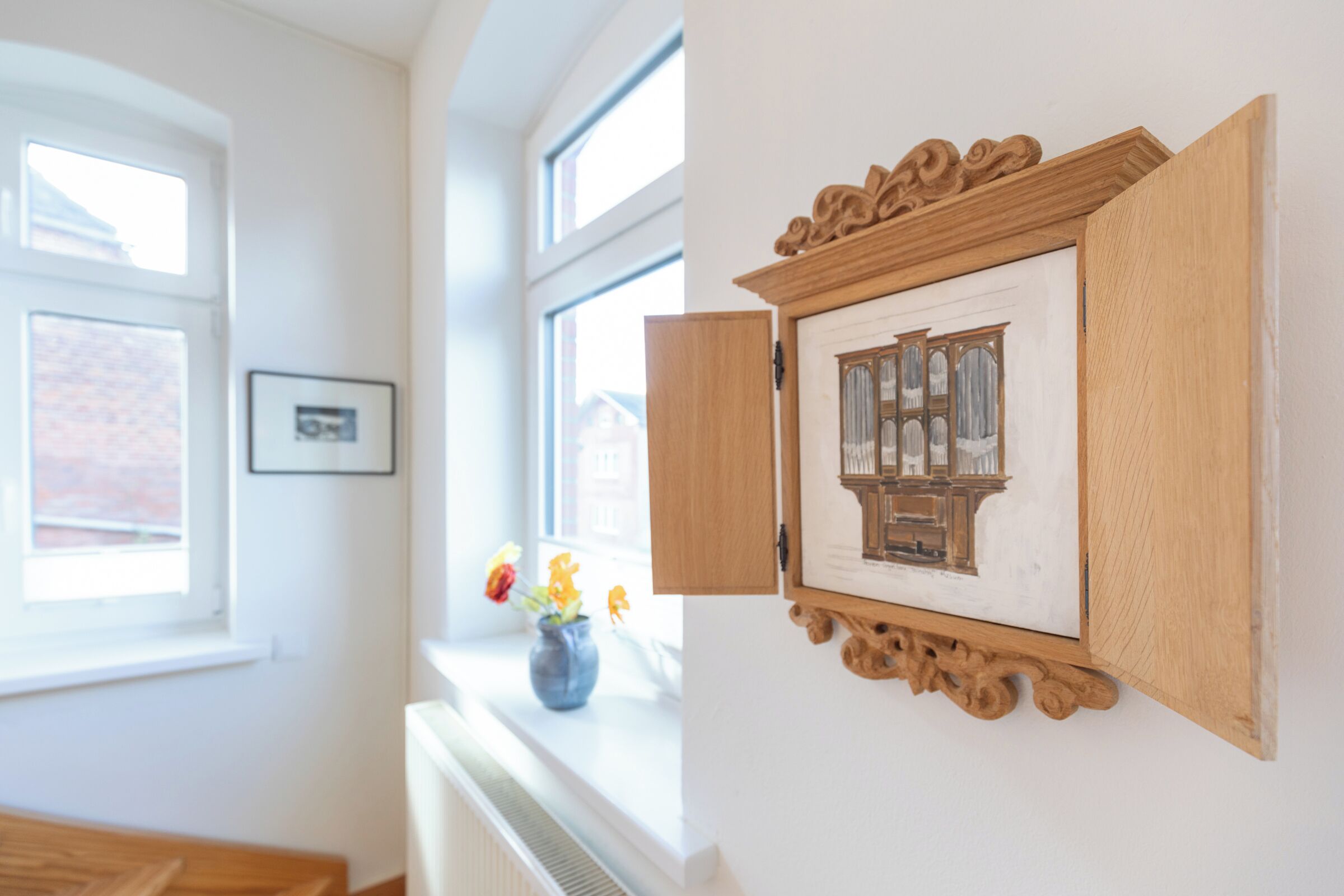 Ein Zimmer mit Fenster, einem gerahmten Bild und einer Blumenvase auf der Fensterbank.