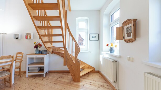 Een trap met houten leuningen die naar een verdieping leidt, een witte radiator en een klein plankje met een bloemenvaas.