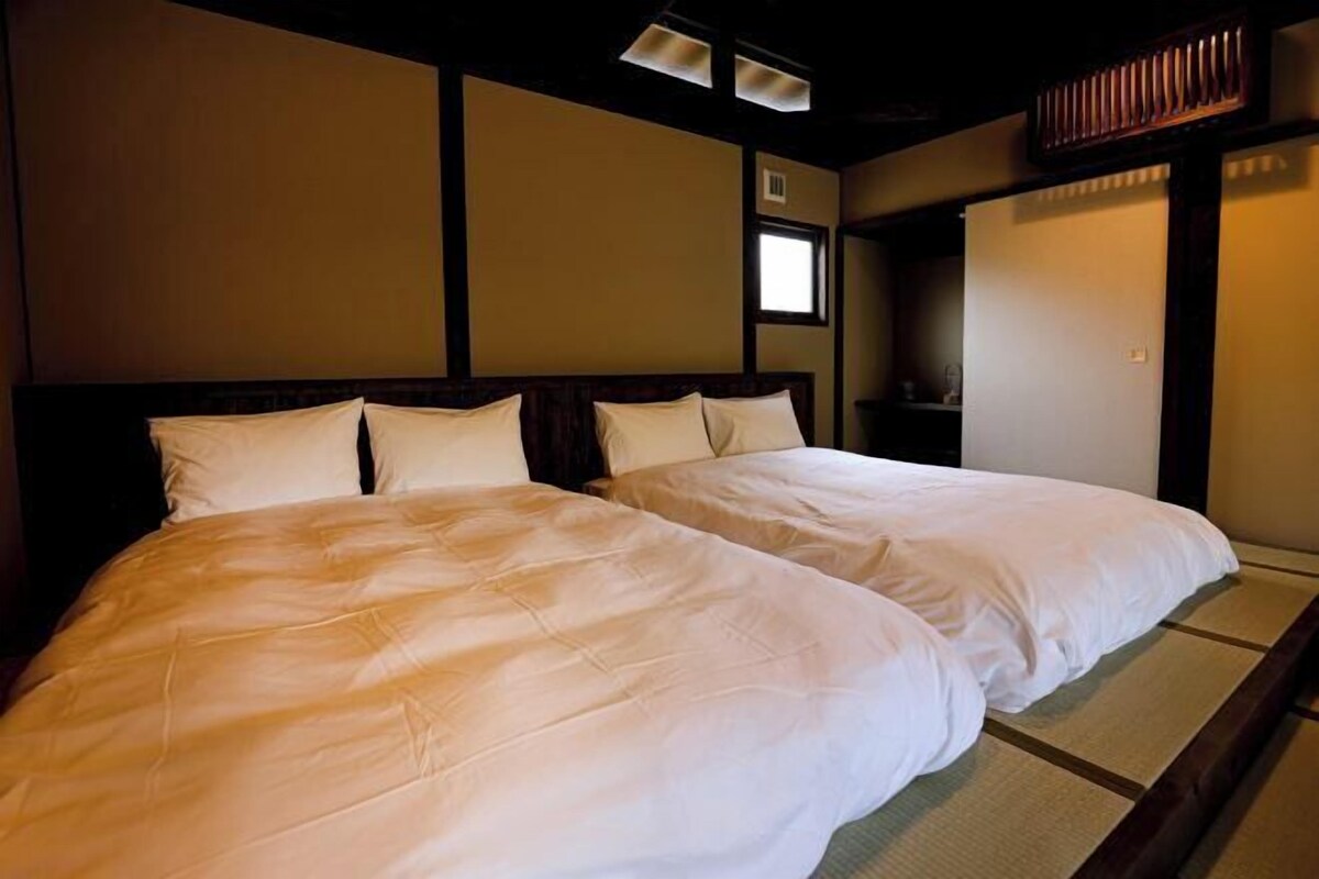 A room with two beds, a wooden headboard, a small window, and a traditional Japanese sliding door.