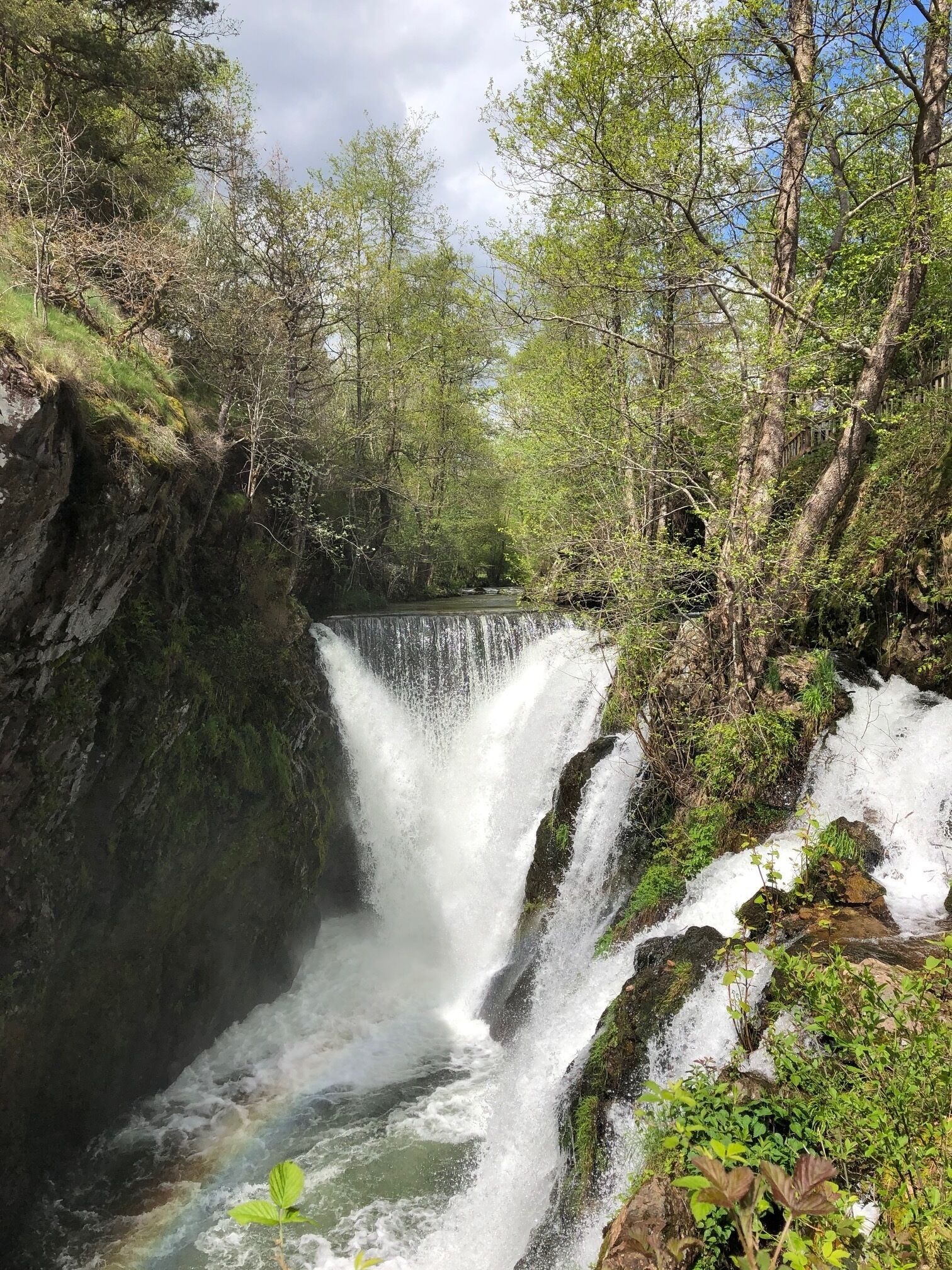 A waterfall surrounded by lush greenery and rocky terrain.