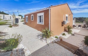 A small, single-story building with a brown exterior and white trim. It features a gravel driveway and a small patio area with outdoor seating. - Lovely home in Villespassans (Villespassans)