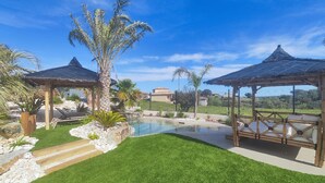 Ein Garten mit Schwimmbad, Palmen und einem Pavillon.